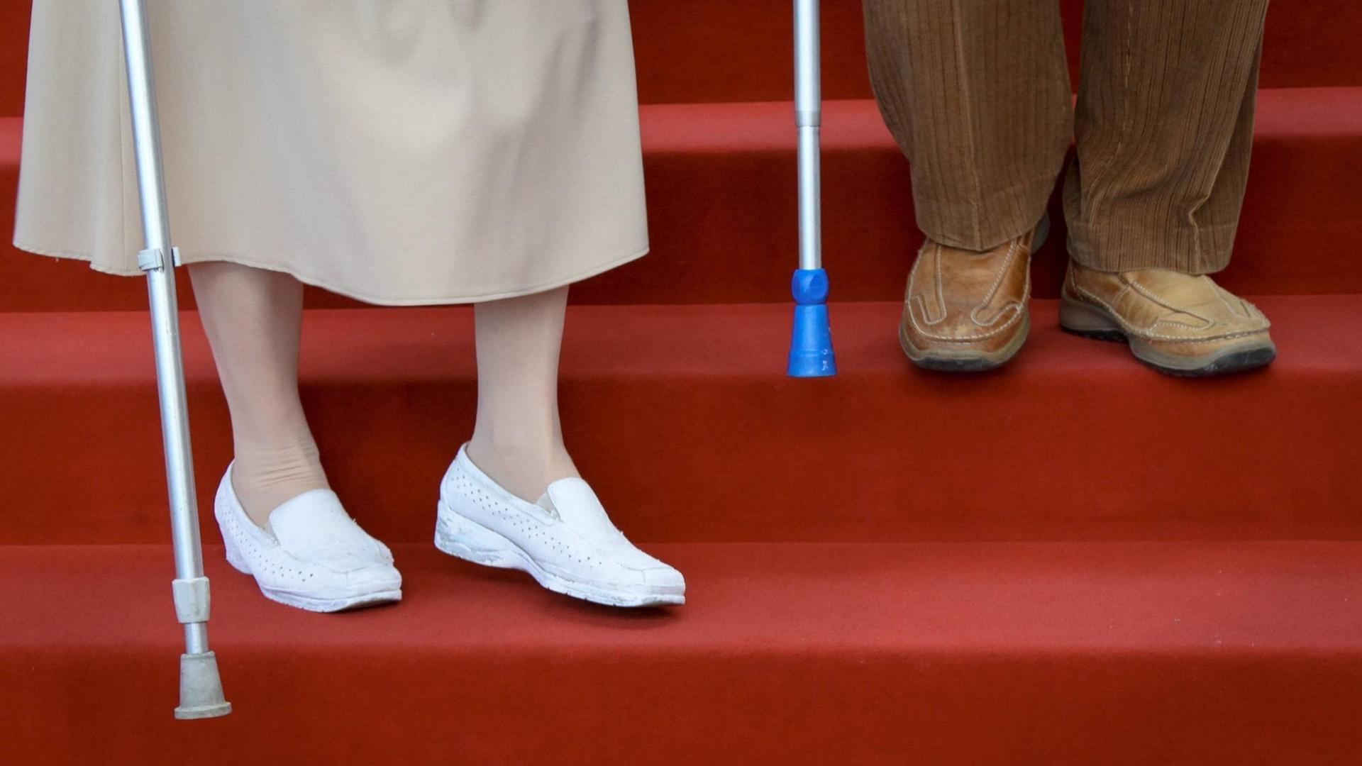 Zwei betagte Senioren steigen eine Treppe mit rotem Teppich herunter. Zwei betagte Senioren steigen eine Treppe mit rotem Teppich herunter.
