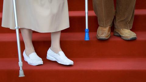Zwei betagte Senioren steigen eine Treppe mit rotem Teppich herunter.