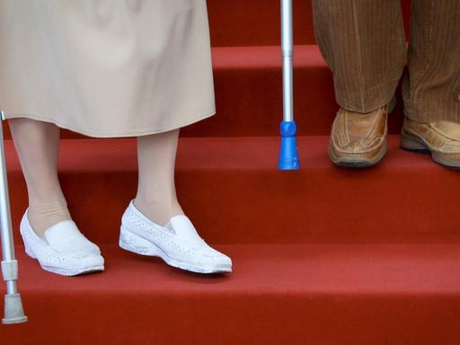 Zwei betagte Senioren steigen eine Treppe mit rotem Teppich herunter.