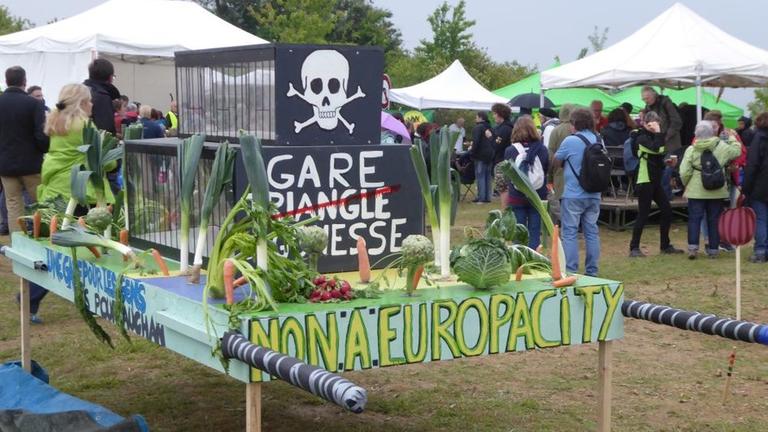 "Nein zu Europa City", steht bei dieser Protestveranstaltung an einem Modell der geplanten Metro-Station Gonesse. Um das Modell steckt Gemüse, wie es auf den umliegenden Feldern wächst.