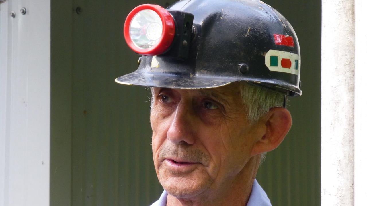Sie sehen einen Mann mit einem dunklen Bergarbeiterhelm auf dem Kopf. An dem Helm ist eine Lampe befestigt. Sie sehen einen Mann mit einem dunklen Bergarbeiterhelm auf dem Kopf. An dem Helm ist eine Lampe befestigt.