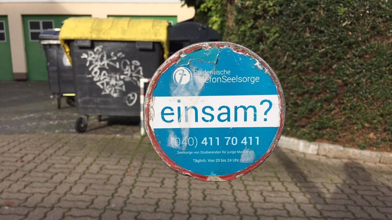 Rundes Metallschild von der Studentischen Telefonseelsorge Hamburg mit der Aufschrift: "Einsam?" und der Telefonnummer. Rundes Metallschild von der Studentischen Telefonseelsorge Hamburg mit der Aufschrift: "Einsam?" und der Telefonnummer.