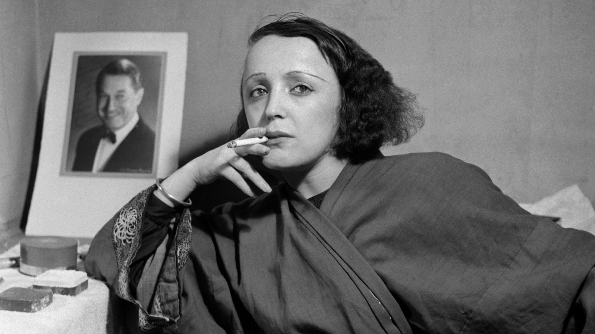Die Sängerin Edith Piaf vor einem Schwarzweiß-Foto von Maurice Chevalier im Jahr 1947. Die Sängerin Edith Piaf vor einem Schwarzweiß-Foto von Maurice Chevalier im Jahr 1947.