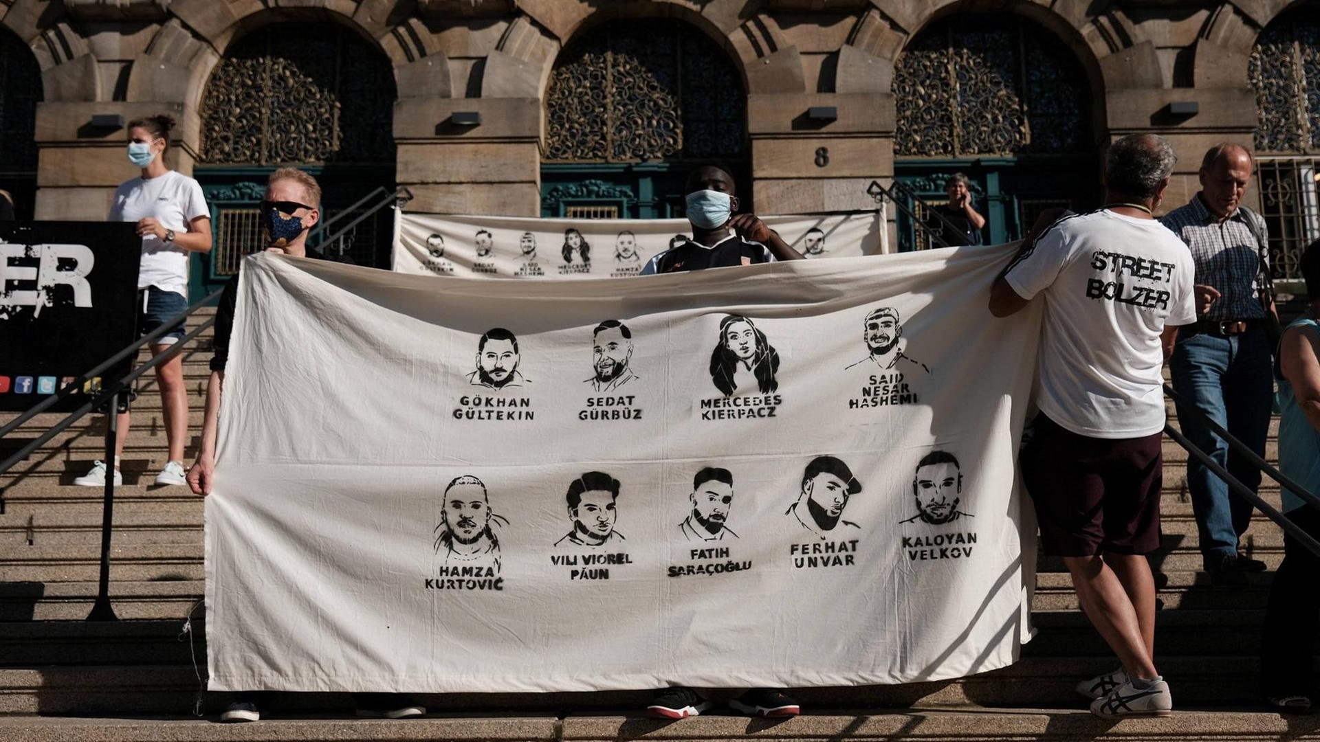 Teilnehmer der Gedenkdemo halten auf Stufen ein Plakat mit den Namen und Gesichtern der Opfer von Hanau Teilnehmer der Gedenkdemo halten auf Stufen ein Plakat mit den Namen und Gesichtern der Opfer von Hanau