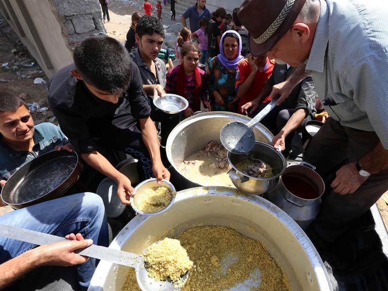Zahlreiche Menschen stehen um zwei große Töpfe, aus denen Essen ausgegeben wird.