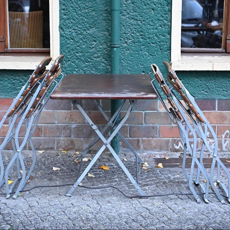 Stühle und Tische stehen zusammengestellt vor einem geschlossenen Restaurant in Berlin.