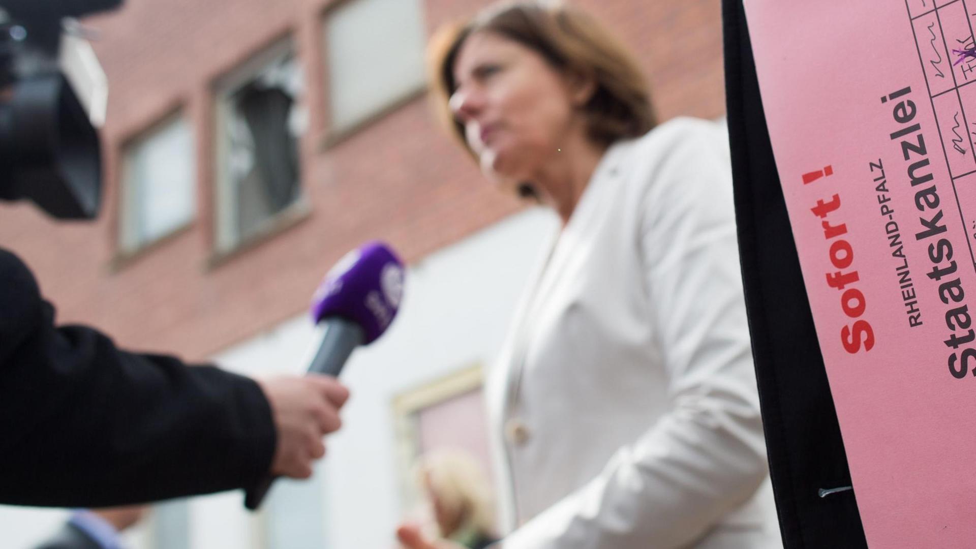 Im Hintergrund ist unscharf die Rheinland-Pfälzische Ministerpräsidentin Malu Dreyer bei einem Fernsehinterview zu sehen, im Vordergrund eine Unterlagenmappe der Staatskanzlei. Im Hintergrund ist unscharf die Rheinland-Pfälzische Ministerpräsidentin Malu Dreyer bei einem Fernsehinterview zu sehen, im Vordergrund eine Unterlagenmappe der Staatskanzlei.