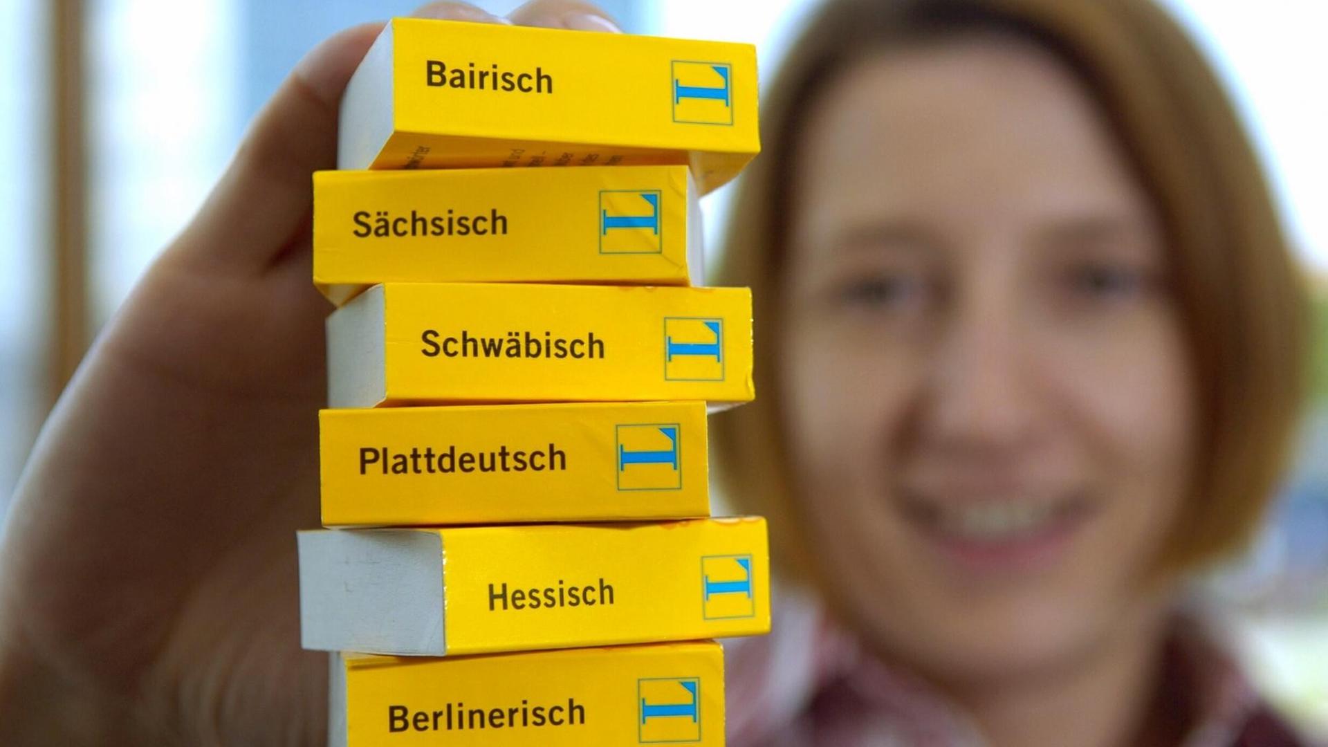 Eine Frau hält einen Stapel Mini-Wörterbücher von Langenscheidt in den Ausgaben Hessisch, Plattdeutsch, Sächsisch, Schwäbisch, Berlinerisch und Bairisch in die Kamera Eine Frau hält einen Stapel Mini-Wörterbücher von Langenscheidt in den Ausgaben Hessisch, Plattdeutsch, Sächsisch, Schwäbisch, Berlinerisch und Bairisch in die Kamera