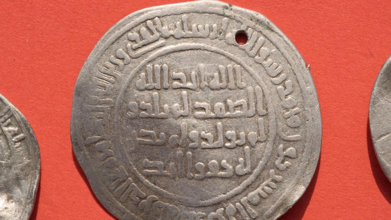 Die älteste, als Anhänger umgearbeitete Münze des Schatzes _ einen Damaskus Dirham - auf das Jahr 714 liegt auf einem Tisch. In einem Acker auf der Ostseeinsel Rügen sind Archäologen auf einen wertvollen skandinavisch dominierten Silberschatz aus dem späten 10. Jahrhundert und damit aus der Umbruchsepoche von der Wikingerzeit zum Christentum gestoßen. Die älteste, als Anhänger umgearbeitete Münze des Schatzes _ einen Damaskus Dirham - auf das Jahr 714 liegt auf einem Tisch. In einem Acker auf der Ostseeinsel Rügen sind Archäologen auf einen wertvollen skandinavisch dominierten Silberschatz aus dem späten 10. Jahrhundert und damit aus der Umbruchsepoche von der Wikingerzeit zum Christentum gestoßen.