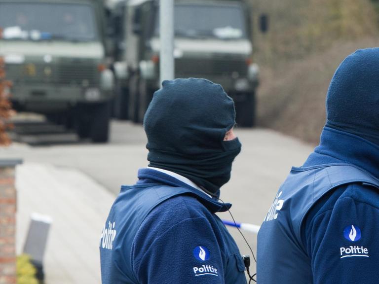 Zwei belgische Sicherheitskräfte gehen bei einem Großeinsatz gegen Islamisten in Kortrijk vor zwei Fahrzeugen her