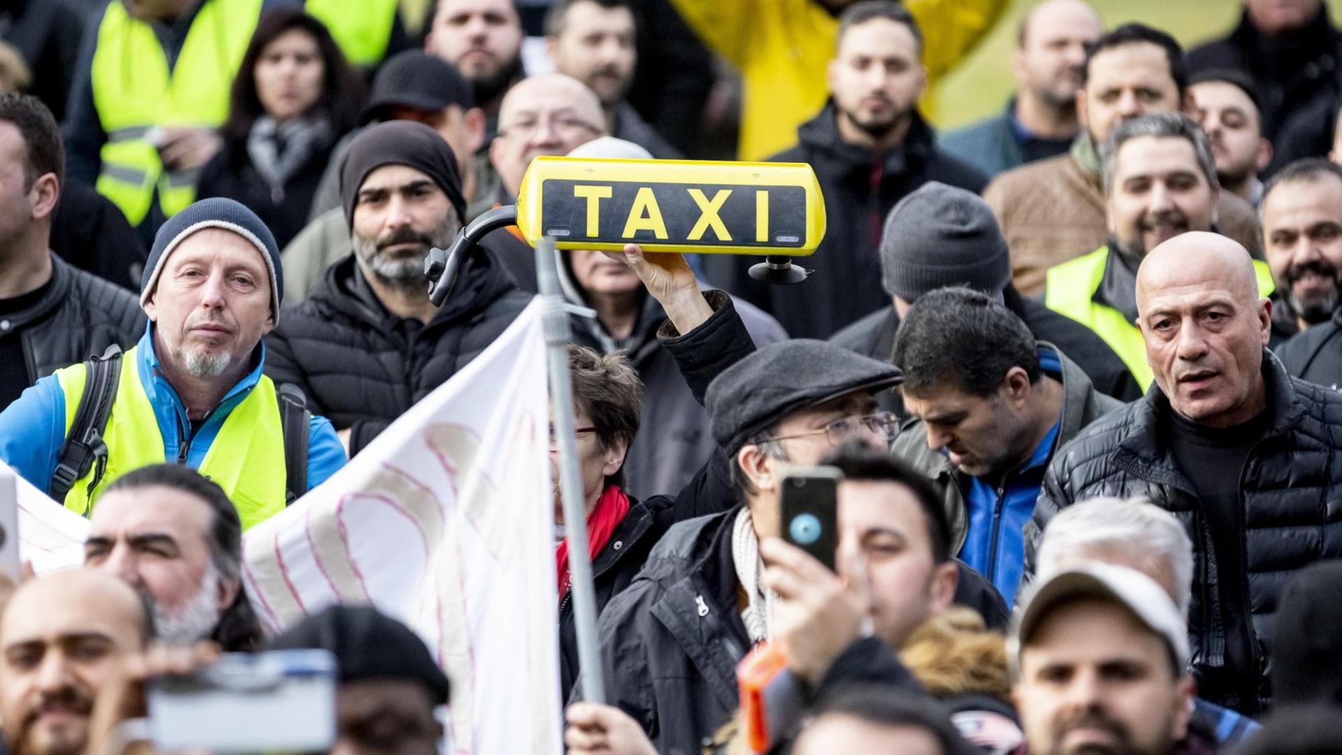 Eine Teilnehmerin hält bei einer Kundgebung von Taxifahrern am Bundesverkehrsministerium ein Taxi-Dachschild in die Höhe. Eine Teilnehmerin hält bei einer Kundgebung von Taxifahrern am Bundesverkehrsministerium ein Taxi-Dachschild in die Höhe.