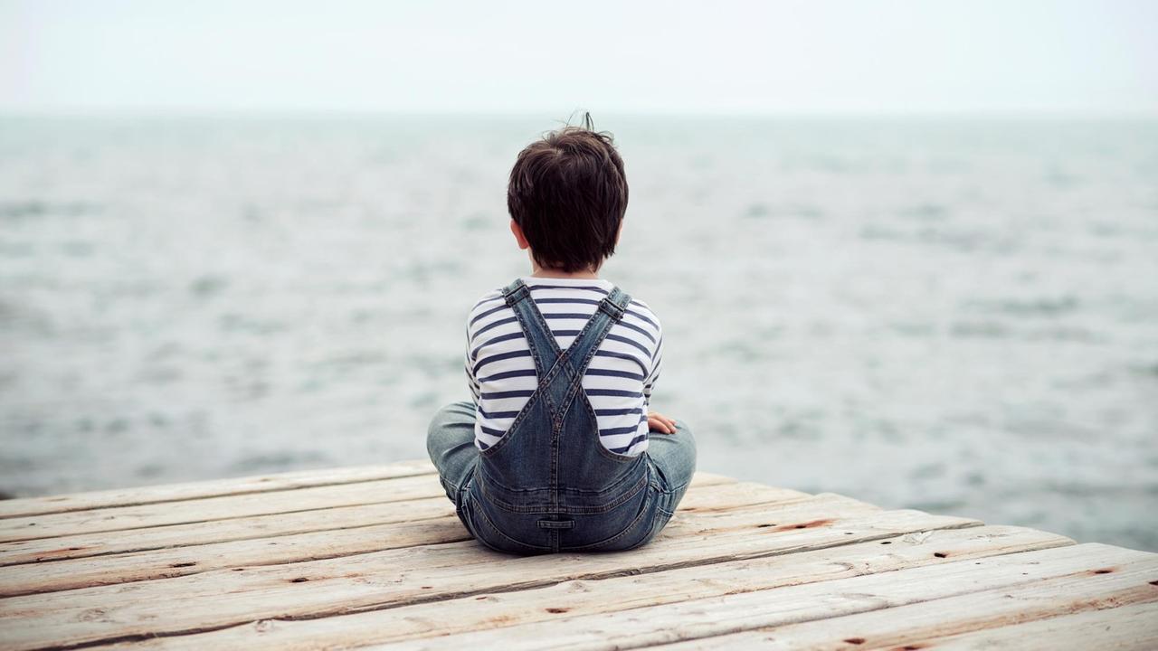 Auf einem Steg sitzt ein kleiner Junge und schaut aufs Meer. Er sieht einsam aus. Auf einem Steg sitzt ein kleiner Junge und schaut aufs Meer. Er sieht einsam aus.