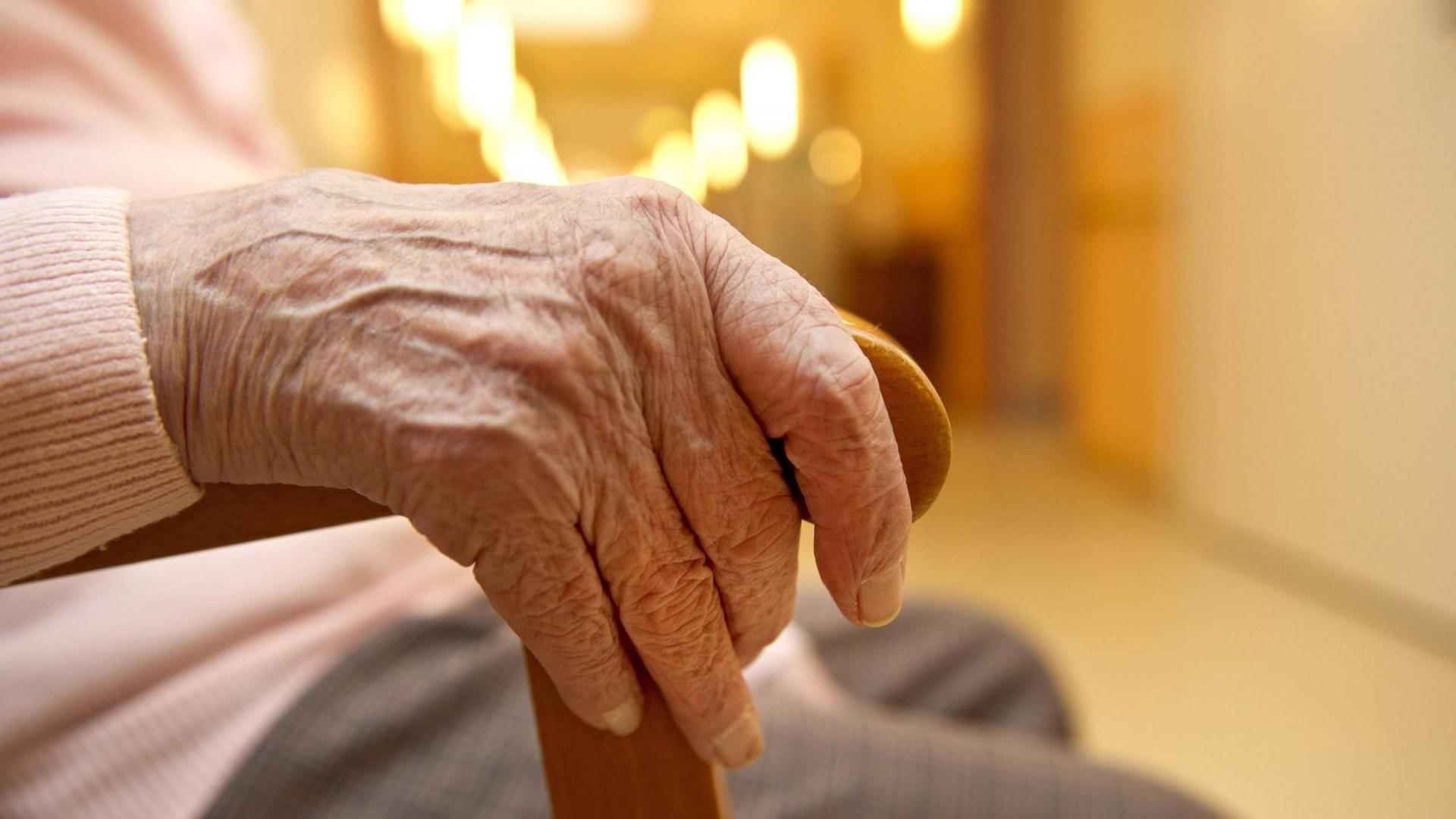 Eine Hand einer älteren Dame umfasst eine Stuhllehne. Eine Hand einer älteren Dame umfasst eine Stuhllehne.