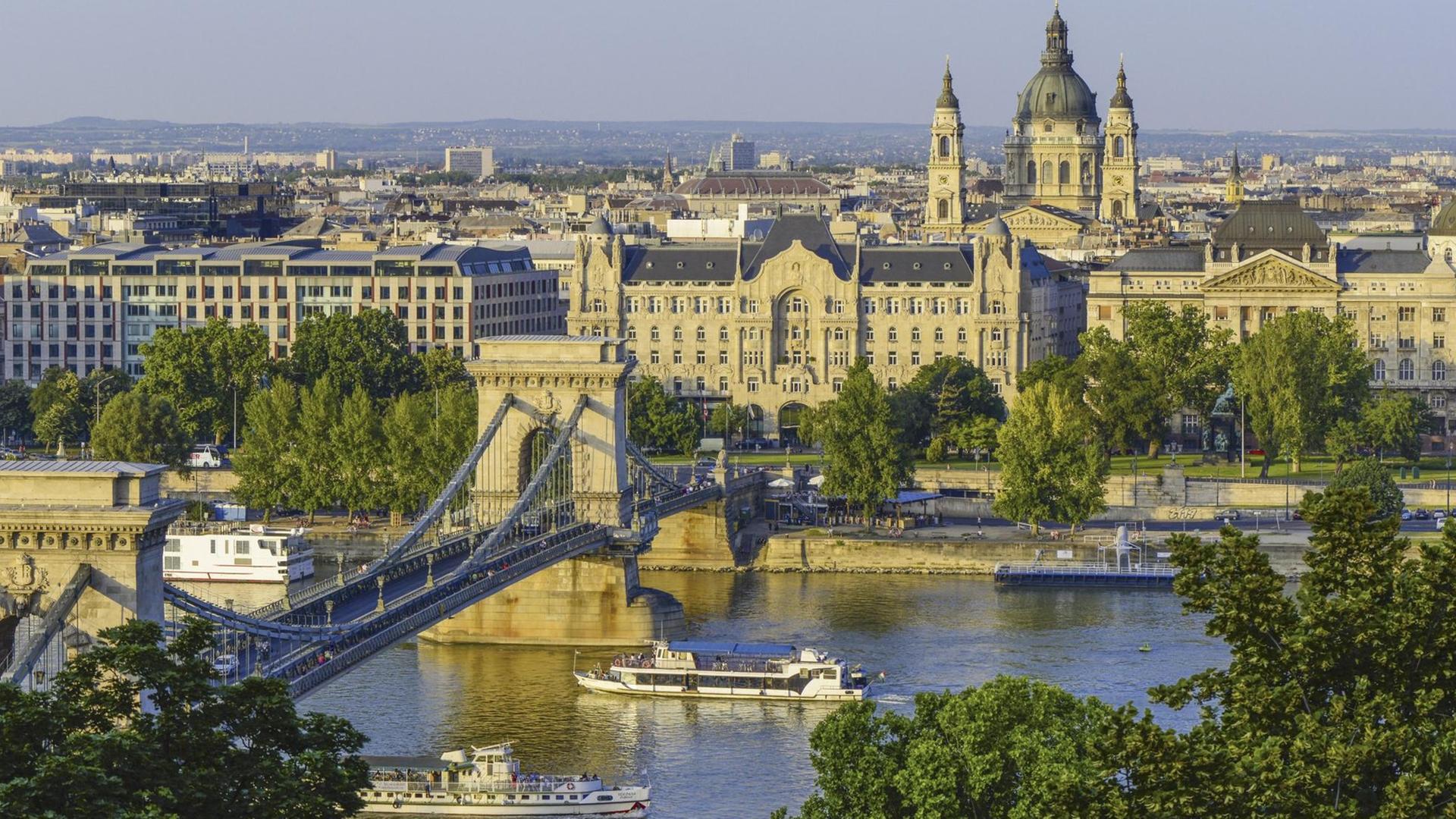Blick auf Budapest von leicht erhöhter Position, im Vordergrund ein breiter Fluss, auf dem zwei Schiffe fahren. Blick auf Budapest von leicht erhöhter Position, im Vordergrund ein breiter Fluss, auf dem zwei Schiffe fahren.