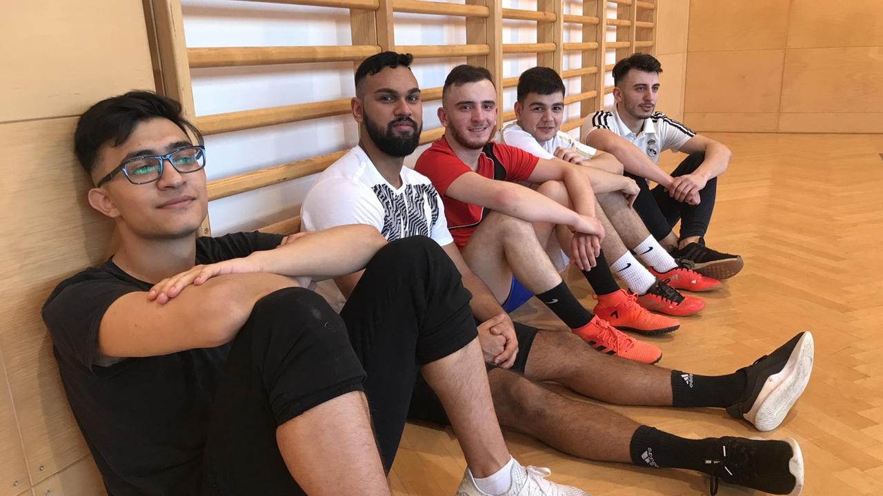 Spieler des "FC International" sitzen in der Turnhalle auf dem Boden. Spieler des "FC International" sitzen in der Turnhalle auf dem Boden.