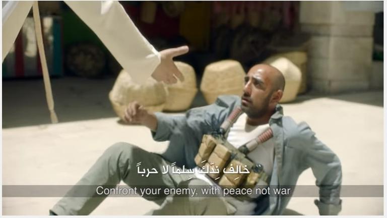 Screenshot eines Youtube-Videos: Ein Mann reicht einem Selbstmord-Attentäter, der einen Sprengstoffgürtel trägt und auf dem Boden liegt, die Hand.