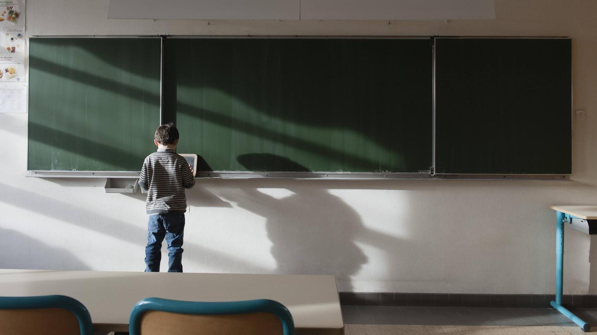 Ein Junge steht an einer Tafel im leeren Klassenraum. Ein Junge steht an einer Tafel im leeren Klassenraum.
