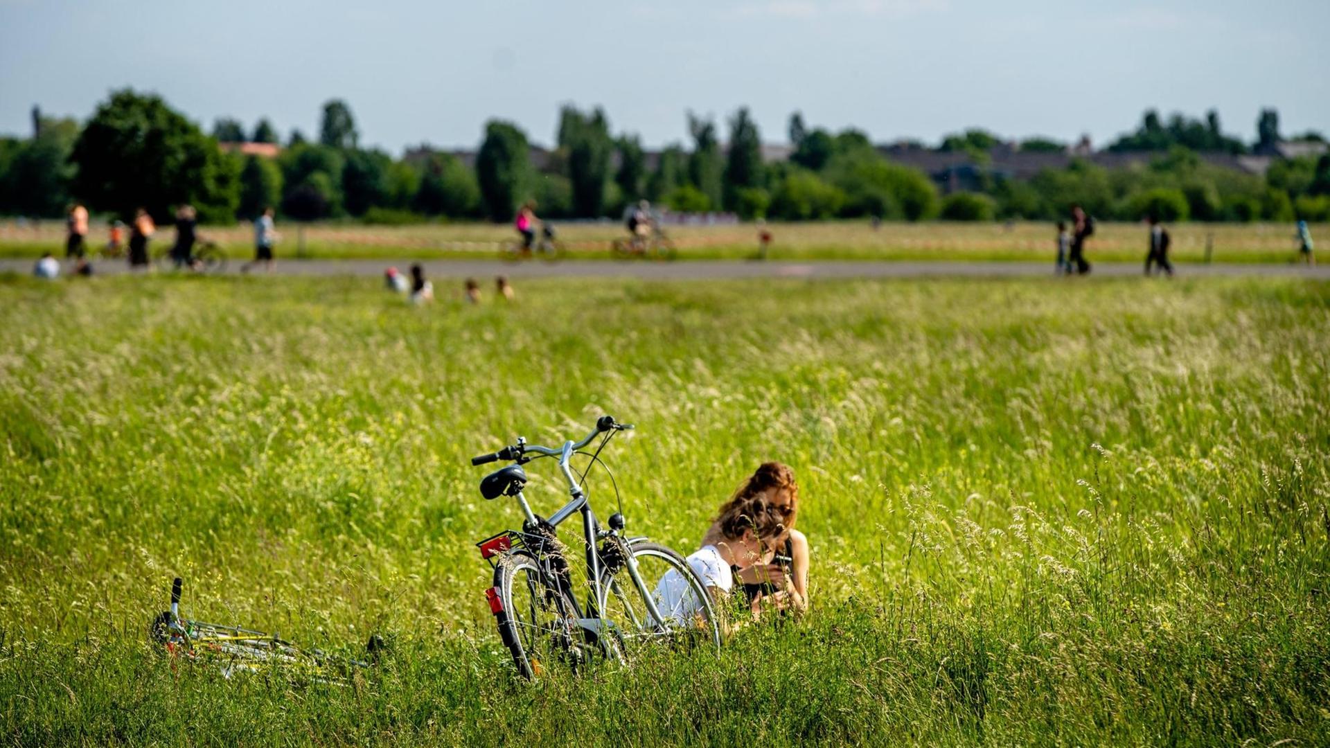 Zwei Menschen sitzen im hohen, grünen Gras, ein Rad steht daneben.