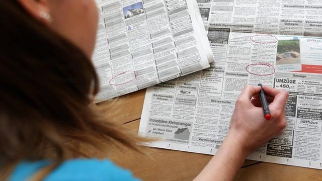Eine Frau umkreist Wohnungsanzeigen in einer Tageszeitung.