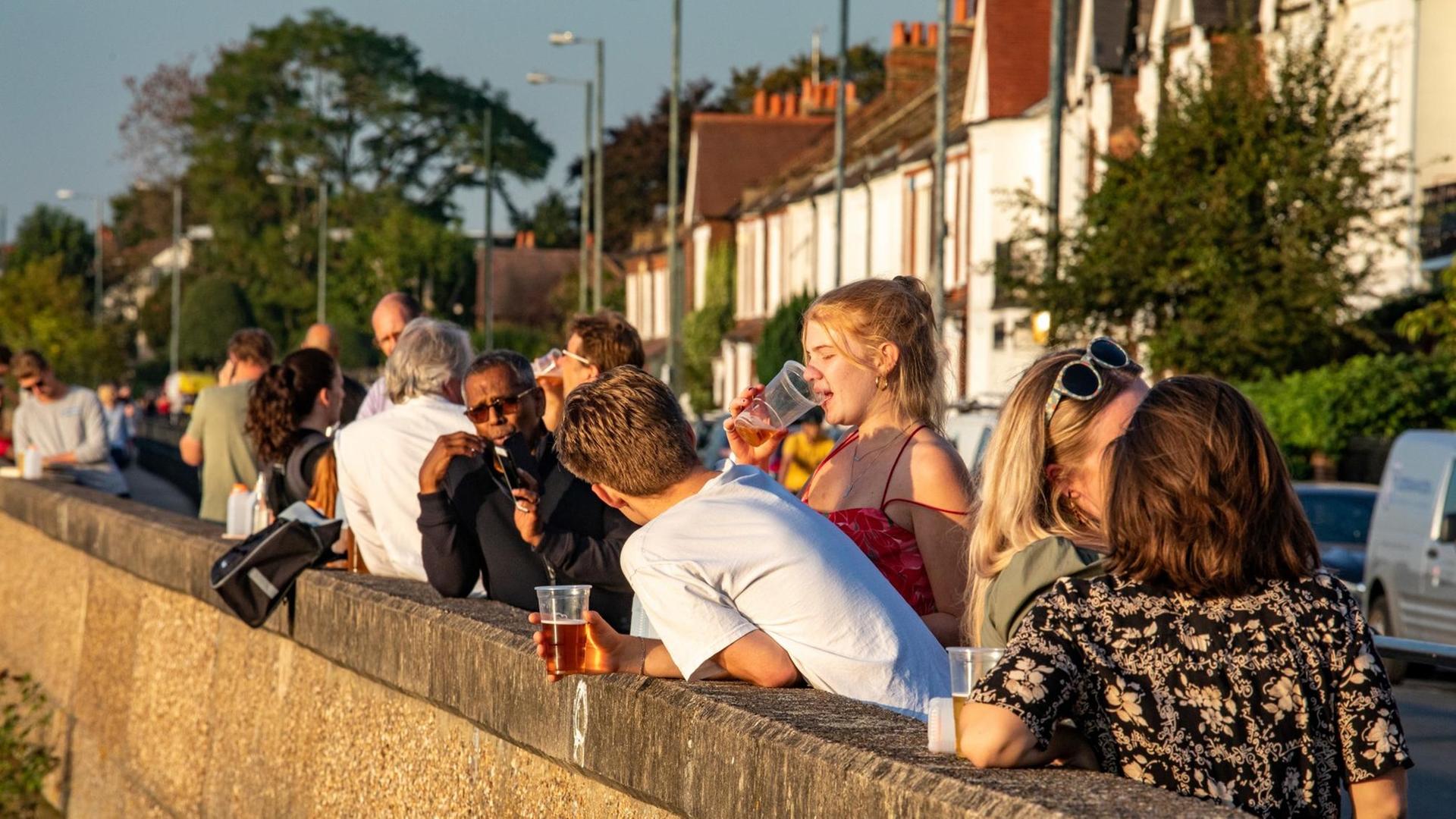 Junge Menschen genießen am Abend ein Bier in der warmen Sonne in Barnes im Südwesten Londons