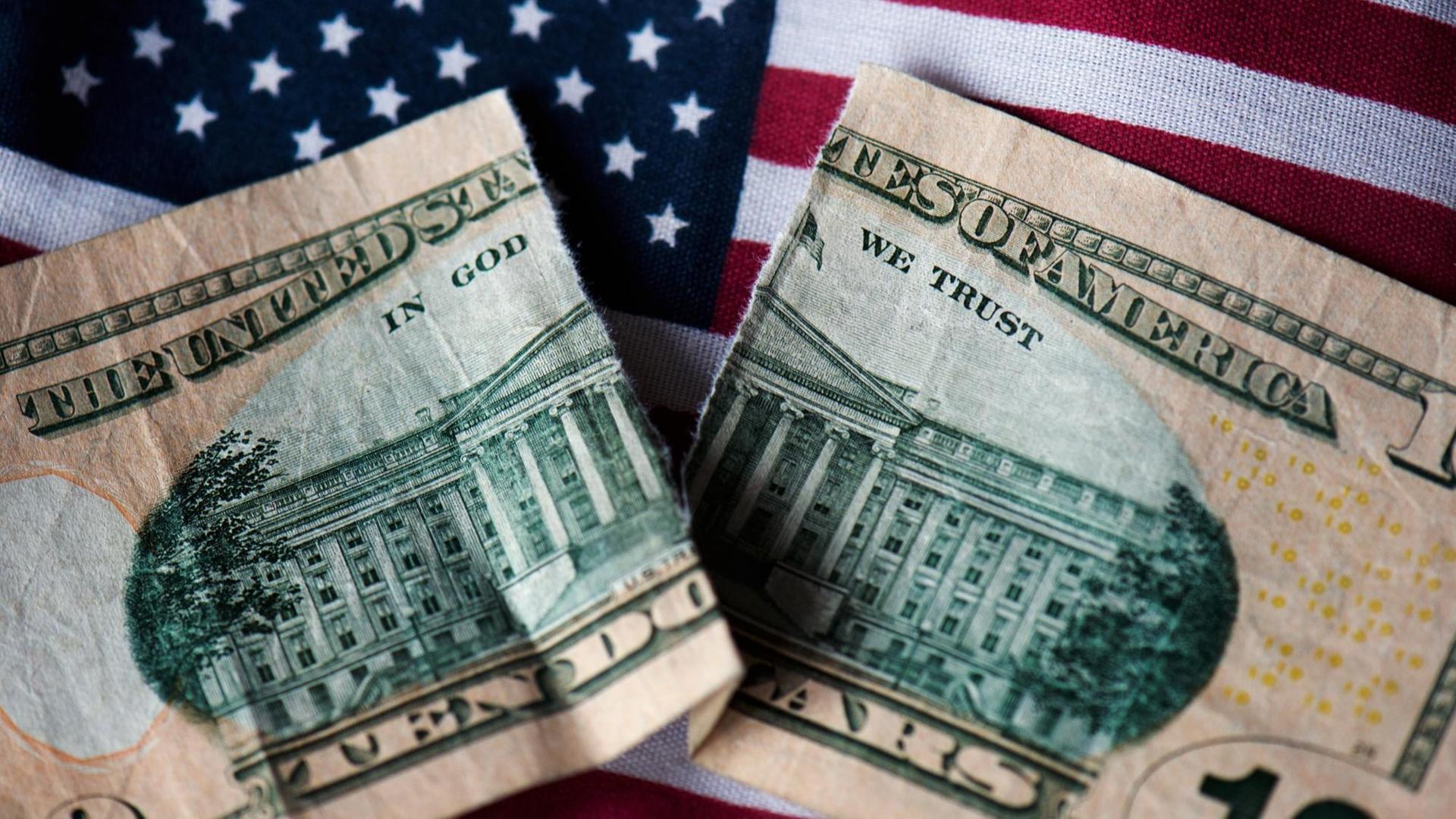 ILLUSTRATION - Auf einer US-amerikanischen Fahne in Dresden (Sachsen) liegt am 16.10.2013 eine zerissene zehn-Dollar-Banknote. Foto: Arno Burgi/dpa | Verwendung weltweit ILLUSTRATION - Auf einer US-amerikanischen Fahne in Dresden (Sachsen) liegt am 16.10.2013 eine zerissene zehn-Dollar-Banknote. Foto: Arno Burgi/dpa | Verwendung weltweit