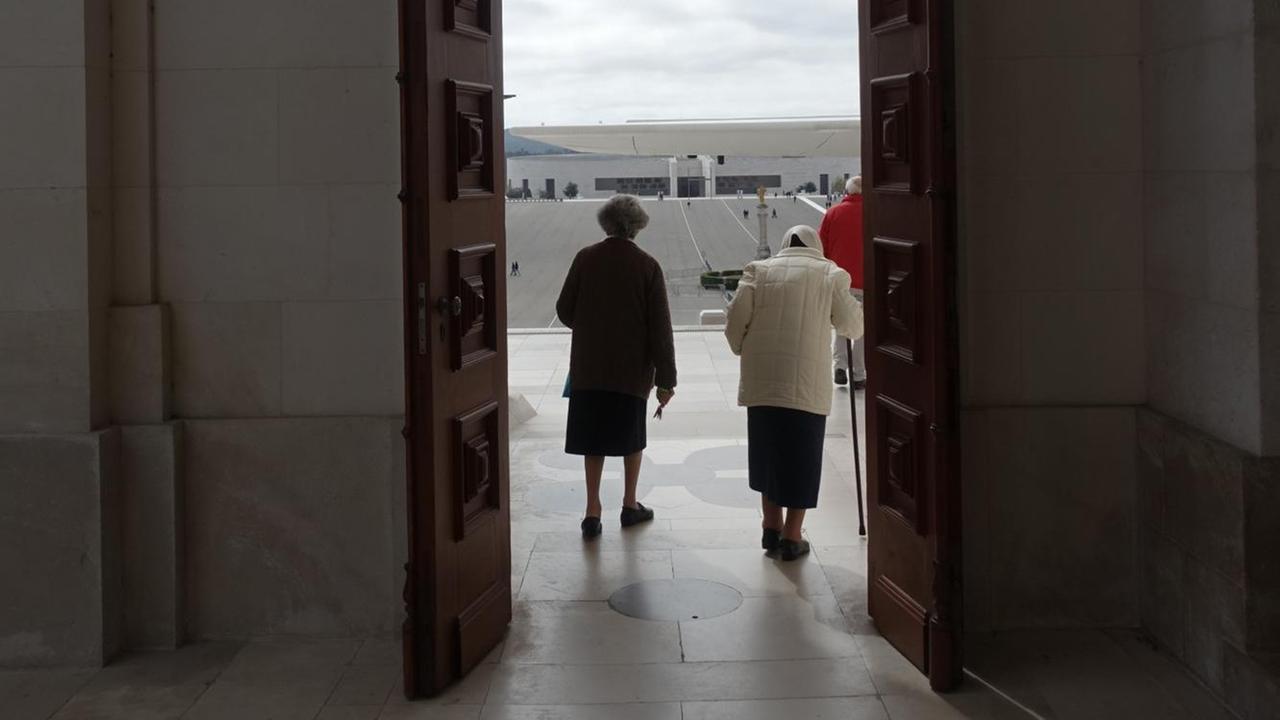 Das Bild zeigt zwei alte Damen, die durch die Tür der Kathedrale von Fátima verlassen.