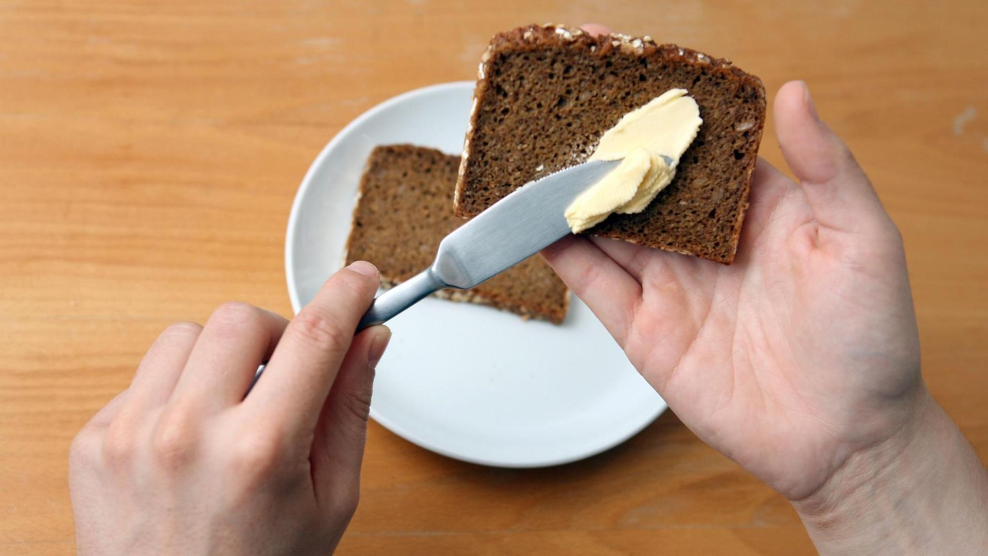 Ein Linkshänder schmiert Butter auf eine Scheibe Brot.