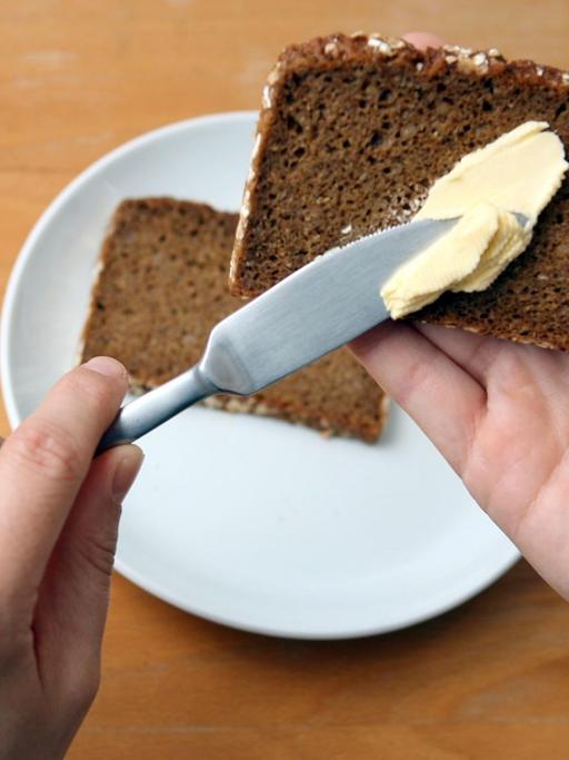 Ein Linkshänder schmiert Butter auf eine Scheibe Brot.