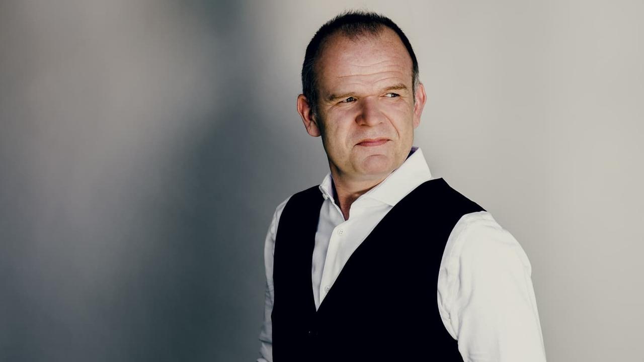 Ein Mann mit weißem Hemd und schwarzer Weste blickt zufrieden zur Seite. Ein Mann mit weißem Hemd und schwarzer Weste blickt zufrieden zur Seite.