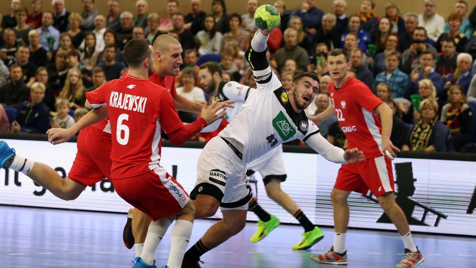 Der deutsche Handball-Spieler Jannik Kohlbacher ist in der Bildmitte zu sehen, wie er sich gegen mehrere Spieler der polnischen Nationalmannschaft durchsetzt. Der deutsche Handball-Spieler Jannik Kohlbacher ist in der Bildmitte zu sehen, wie er sich gegen mehrere Spieler der polnischen Nationalmannschaft durchsetzt.