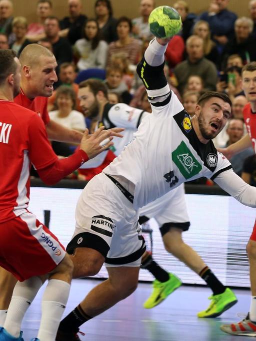 Der deutsche Handball-Spieler Jannik Kohlbacher ist in der Bildmitte zu sehen, wie er sich gegen mehrere Spieler der polnischen Nationalmannschaft durchsetzt.