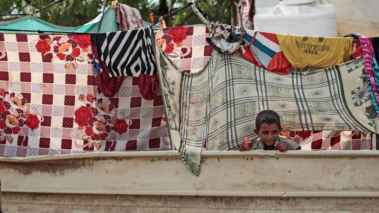 Ein binnenvertriebener jemenitischer Junge schaut vor der Hütte seiner Familie in der Hafenstadt al-Hodeida durch aufgehängte Wäsche.