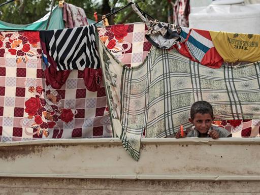 Ein binnenvertriebener jemenitischer Junge schaut vor der Hütte seiner Familie in der Hafenstadt al-Hodeida durch aufgehängte Wäsche.