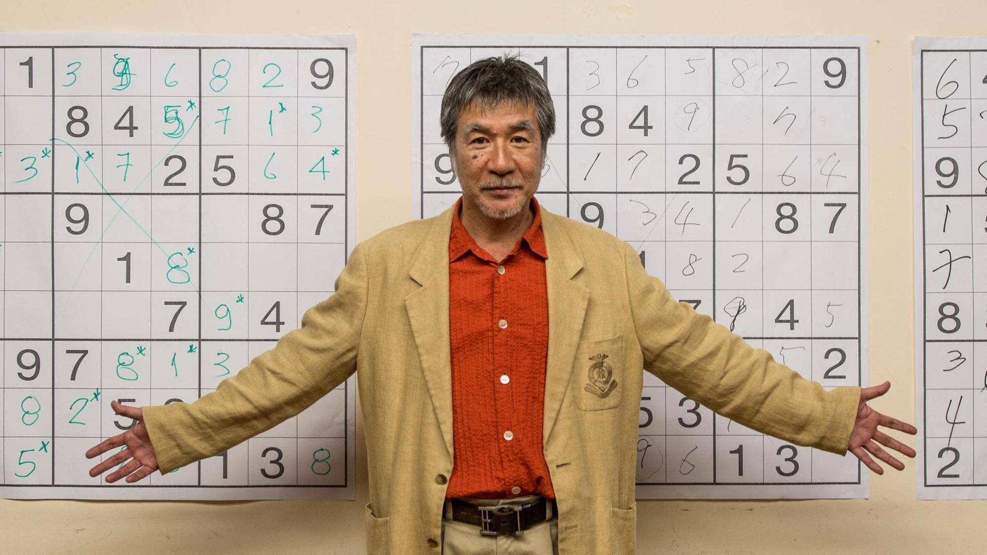 Maki Kaji steht vor einer Wand mit vergrößerten Sudoku-Rätseln.