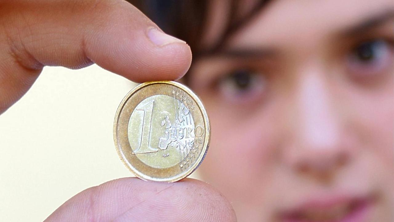Ein junger Mann hält eine Euro-Münze zwischen den Fingern Ein junger Mann hält eine Euro-Münze zwischen den Fingern