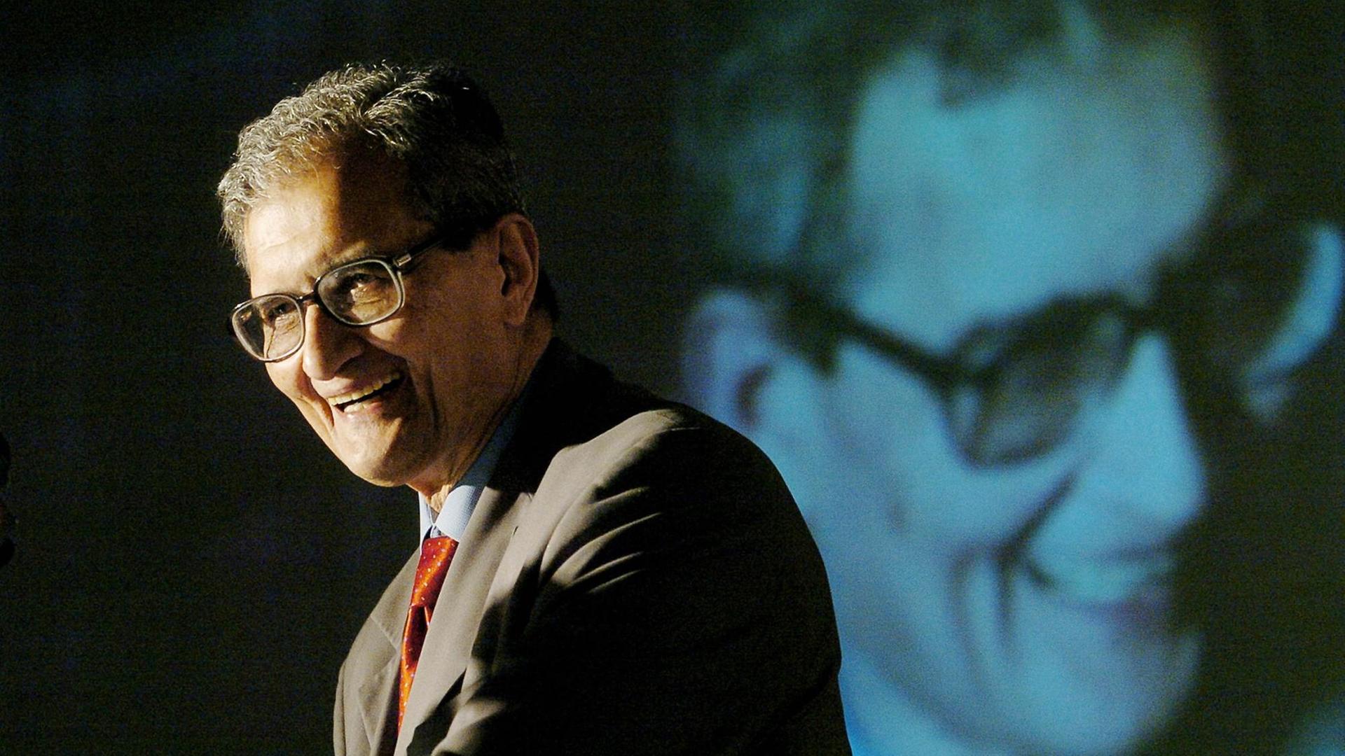 Amartya Sen hält eine Rede, im Hintergund wird sein Gesicht eingeblendet. Amartya Sen hält eine Rede, im Hintergund wird sein Gesicht eingeblendet.