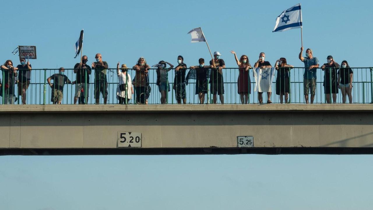 Auf einer Autobahnbrücke stehen Menschen und schwenken die israelische Flagge. Auf einer Autobahnbrücke stehen Menschen und schwenken die israelische Flagge.