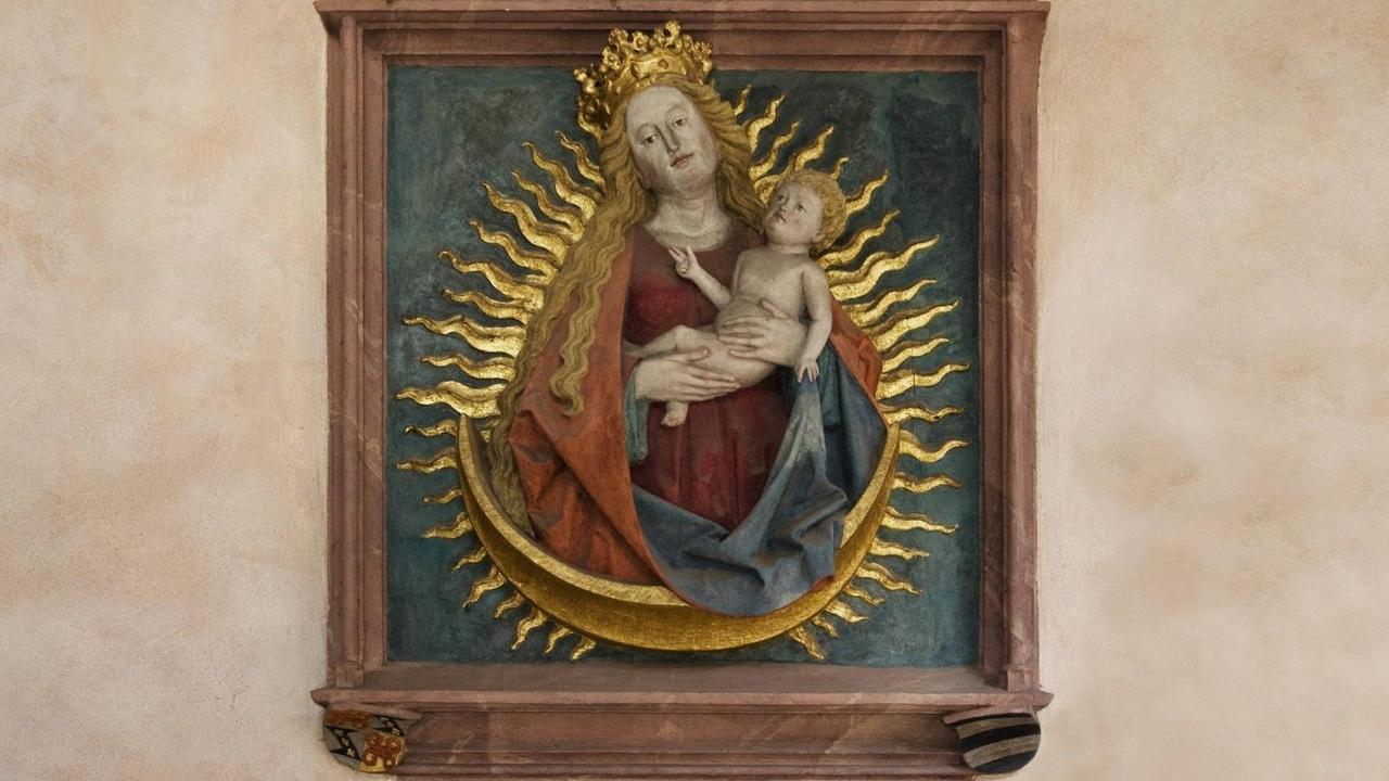 Ein Relief zeigt Maria und das Jesuskind von goldenen Strahlflammen umgeben. Ein Relief zeigt Maria und das Jesuskind von goldenen Strahlflammen umgeben.