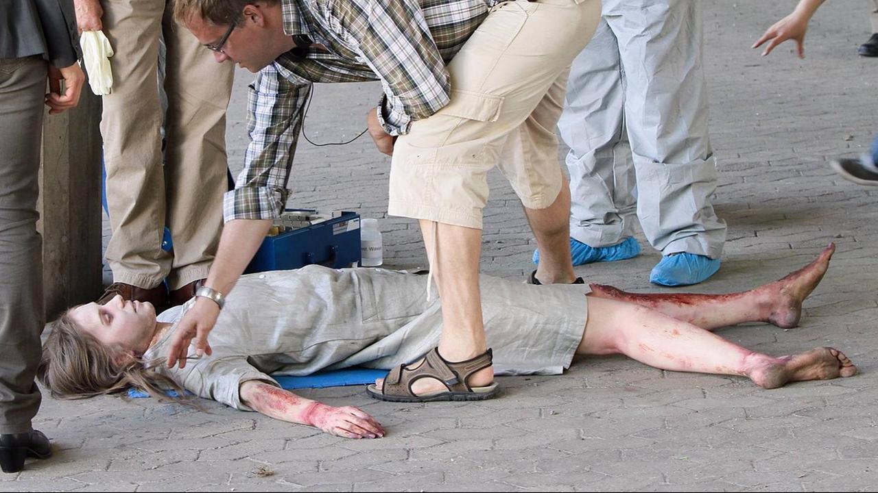 Eine, als Leiche auf dem Boden liegende Darstellerin, erhält Anweisungen vom Regisseur.