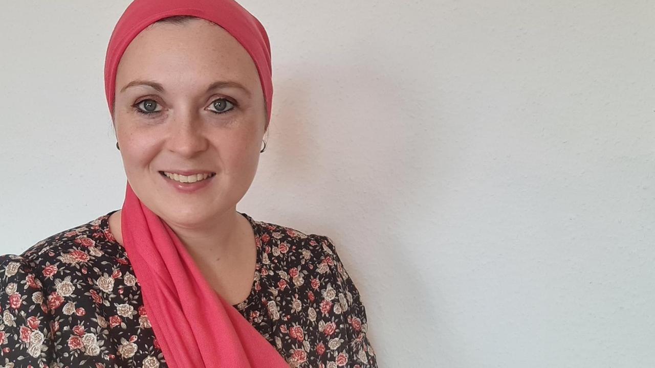 Eine Frau mit rotem Kopftuch steht vor einer weißen Wand und lächelt in die Kamera Eine Frau mit rotem Kopftuch steht vor einer weißen Wand und lächelt in die Kamera