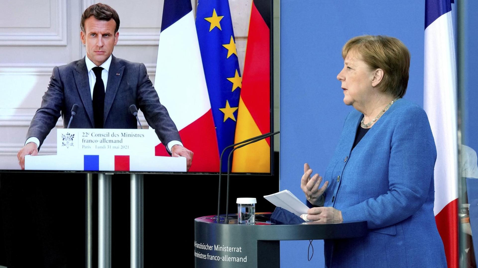 Die Geheim-Dienste von den Ländern Dänemark und USA haben deutsche und europäische Politiker abgehört. Darunter sind auch: Bundes-Kanzlerin Angela Merkel und der französische Staats-Präsident Macron stehen an einem Redner-Tisch.