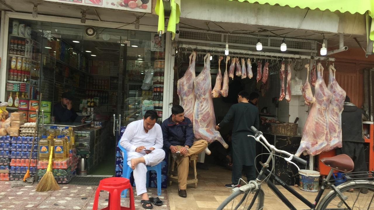 Blick auf kleine Läden in Kabul. In der Auslage hängen große Stücke Fleisch an Haken. Vor dem benachbarten Geschäft sind Getränkekisten aufgebaut. Blick auf kleine Läden in Kabul. In der Auslage hängen große Stücke Fleisch an Haken. Vor dem benachbarten Geschäft sind Getränkekisten aufgebaut.