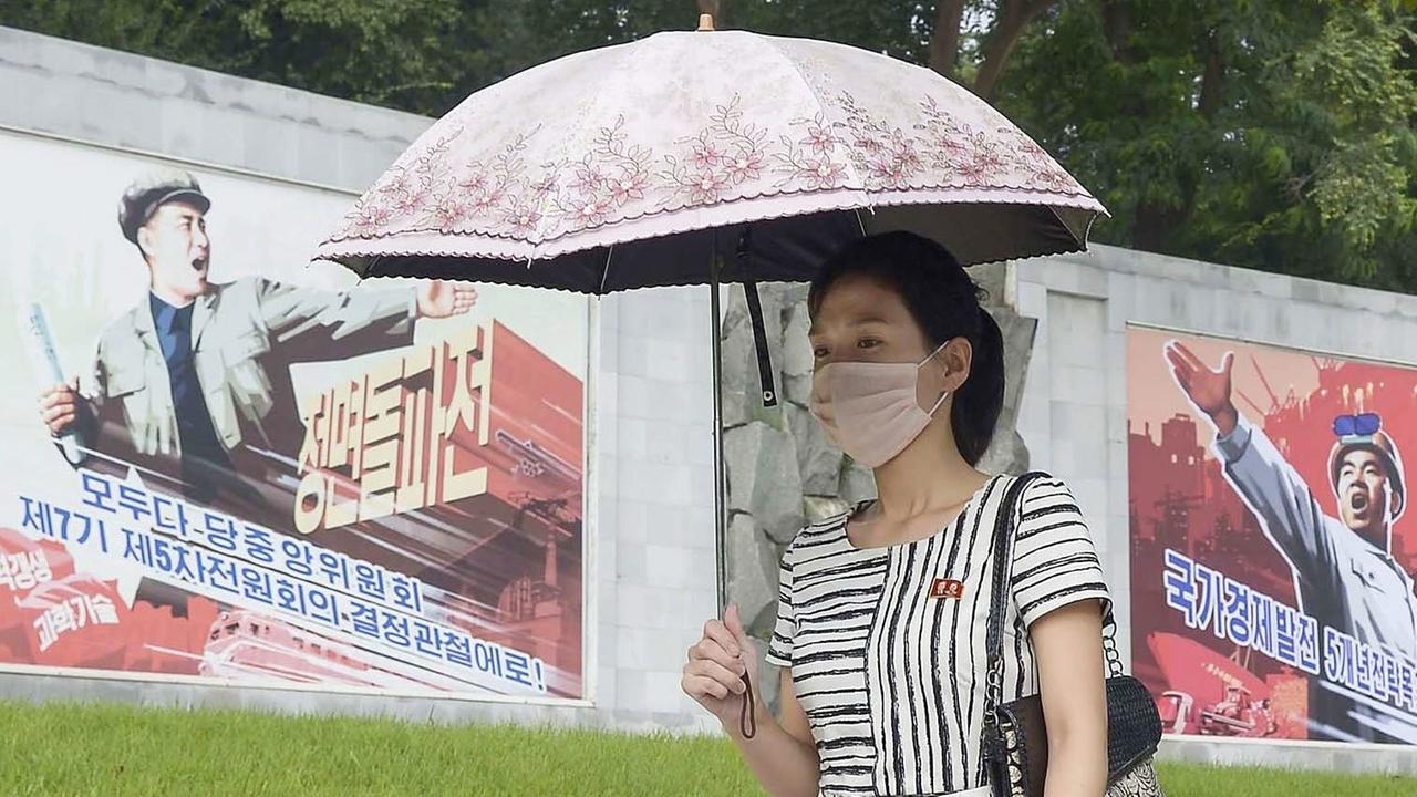 Eine Frau geht mit einer Maske in Pjöngjang an Propaganda-Wandbildern vorbei
