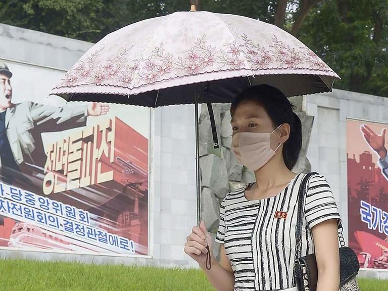 Eine Frau geht mit einer Maske in Pjöngjang an Propaganda-Wandbildern vorbei
