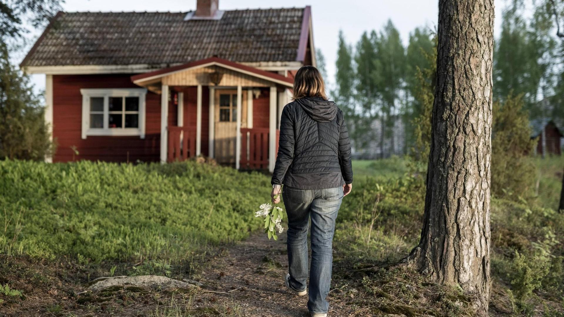 Eine Frau geht auf eine rote Holzhütte im Wald bei Kuopio in Finnland zu