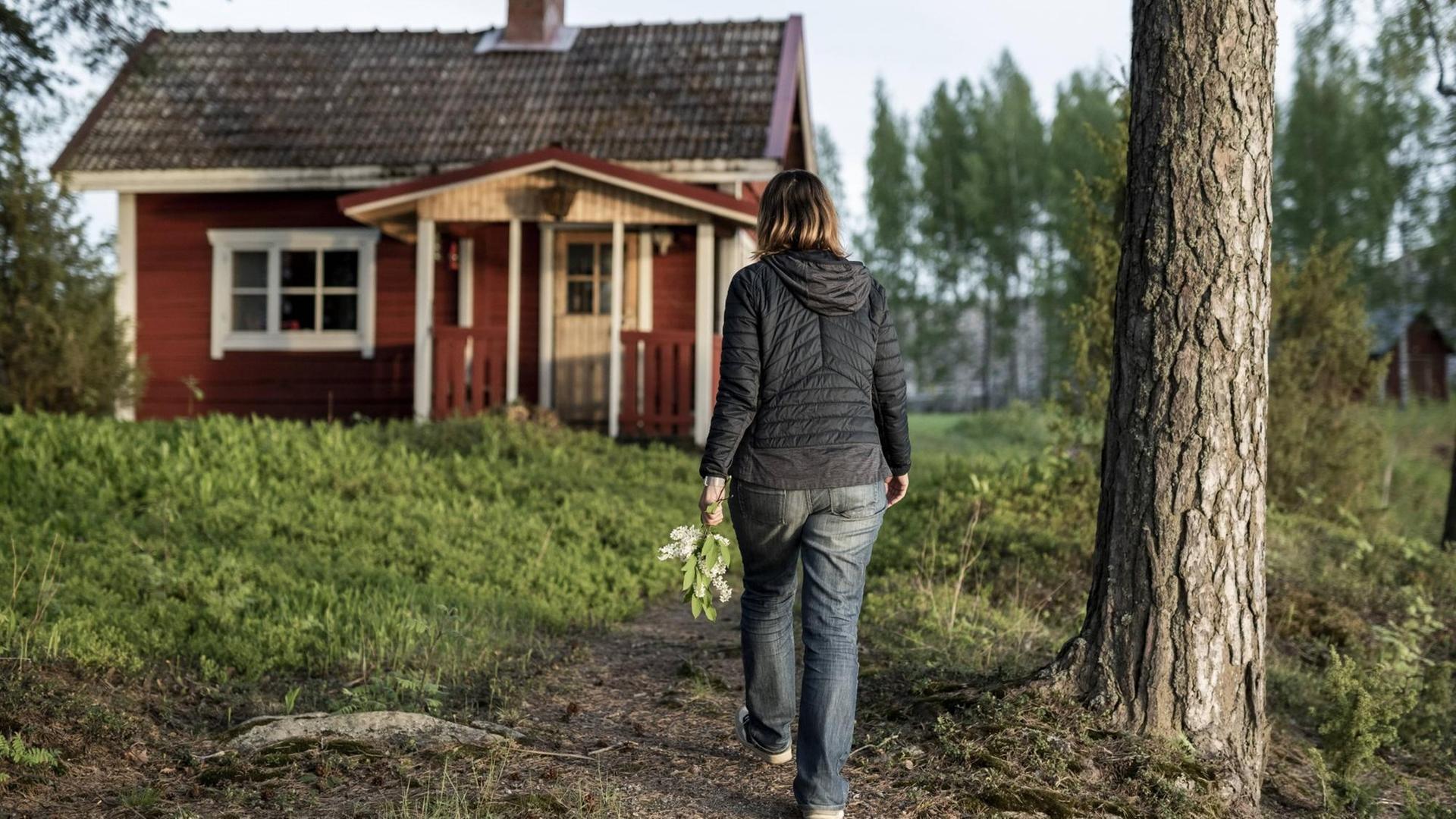 Eine Frau geht auf eine rote Holzhütte im Wald bei Kuopio in Finnland zu Eine Frau geht auf eine rote Holzhütte im Wald bei Kuopio in Finnland zu