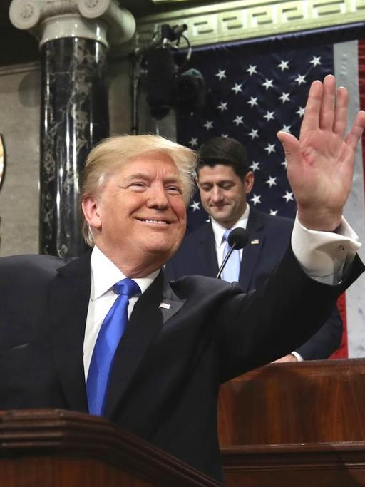 Trump winkt im Abgeordnetenhaus vom Rednerpult aus in den Saal.
