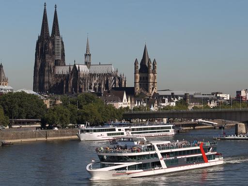 Ein Schiff fährt in Köln am Dom vorbei über den Rhein.