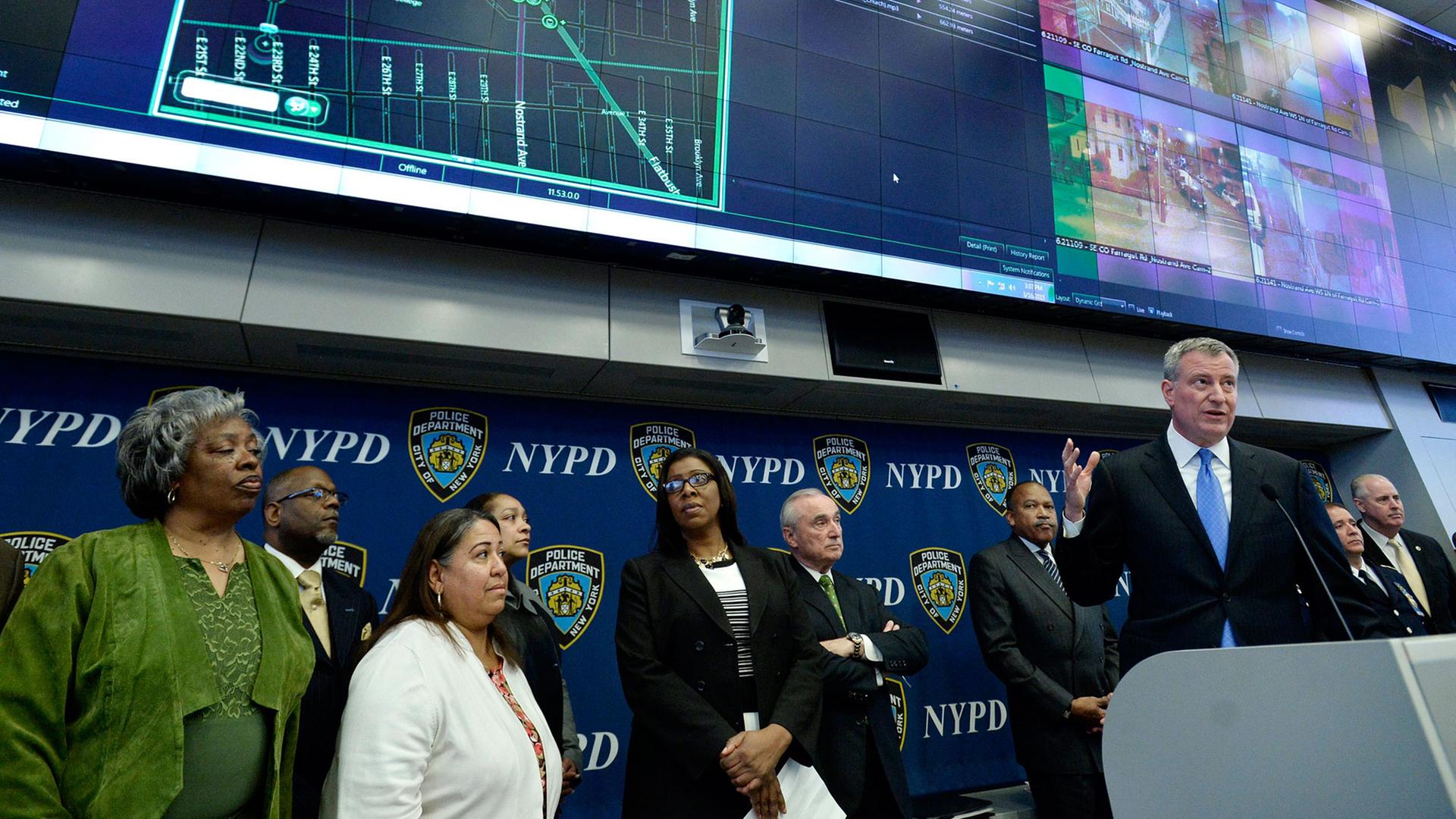 New Yorks Bürgermeister Bill de Blasio (r.) spricht auf einer Pressekonferenz über das neue akustische Überwachungssystem "ShotSpotter". Um ihn herum stehen unter anderem Polizeibeamte. New Yorks Bürgermeister Bill de Blasio (r.) spricht auf einer Pressekonferenz über das neue akustische Überwachungssystem "ShotSpotter". Um ihn herum stehen unter anderem Polizeibeamte.