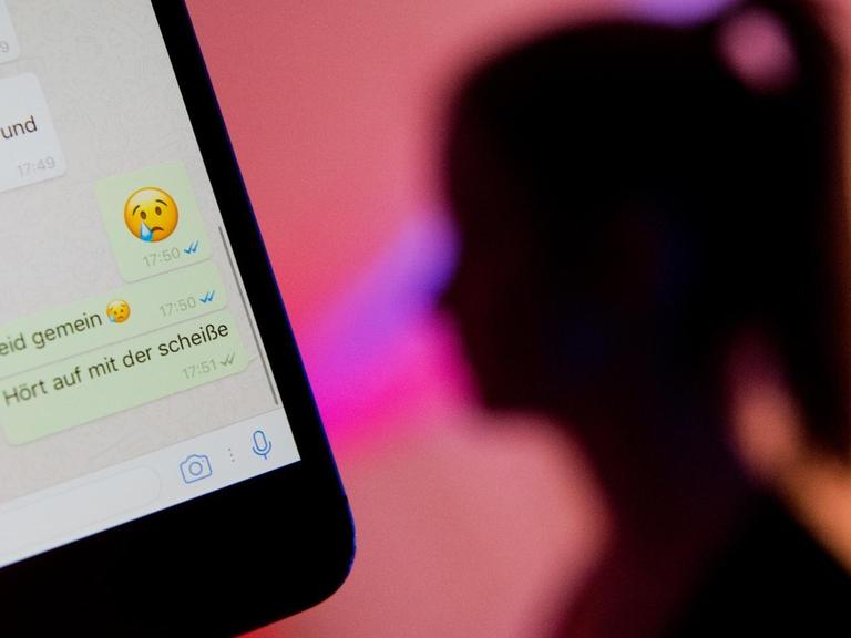 Ein junges Mädchen zeigt das Display eines Smartphones mit einem fiktiven Chatverlauf beim Messenger "WhatsApp".